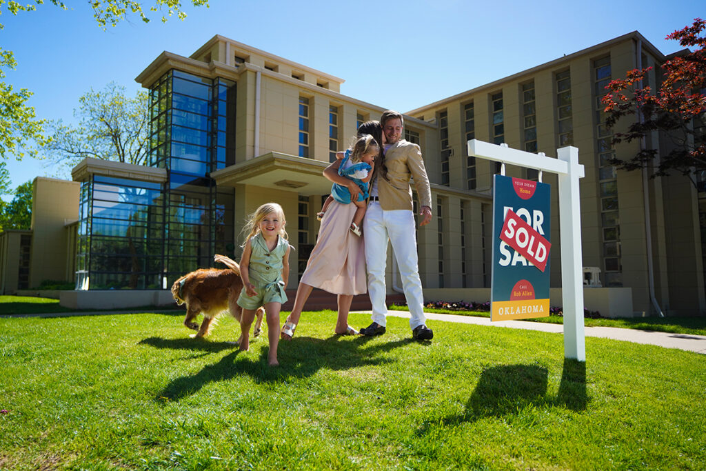 Family with young children and dog play in front yard of a home with a yard sign that says "sold".