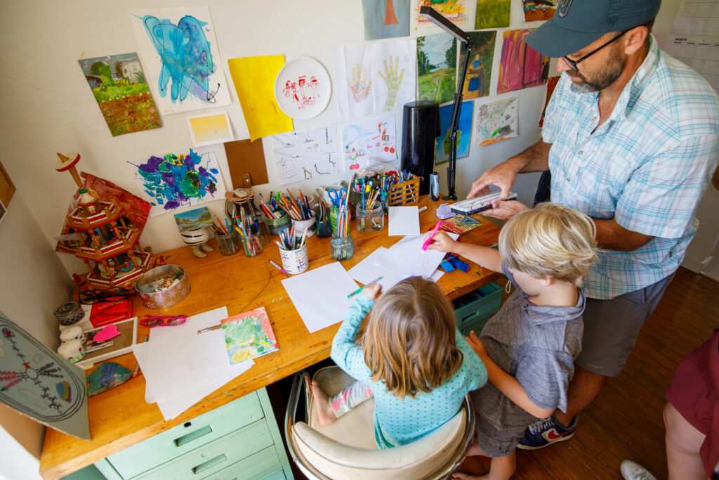 Bryan with two young kids at an arts and crafts table working on various art projects together.