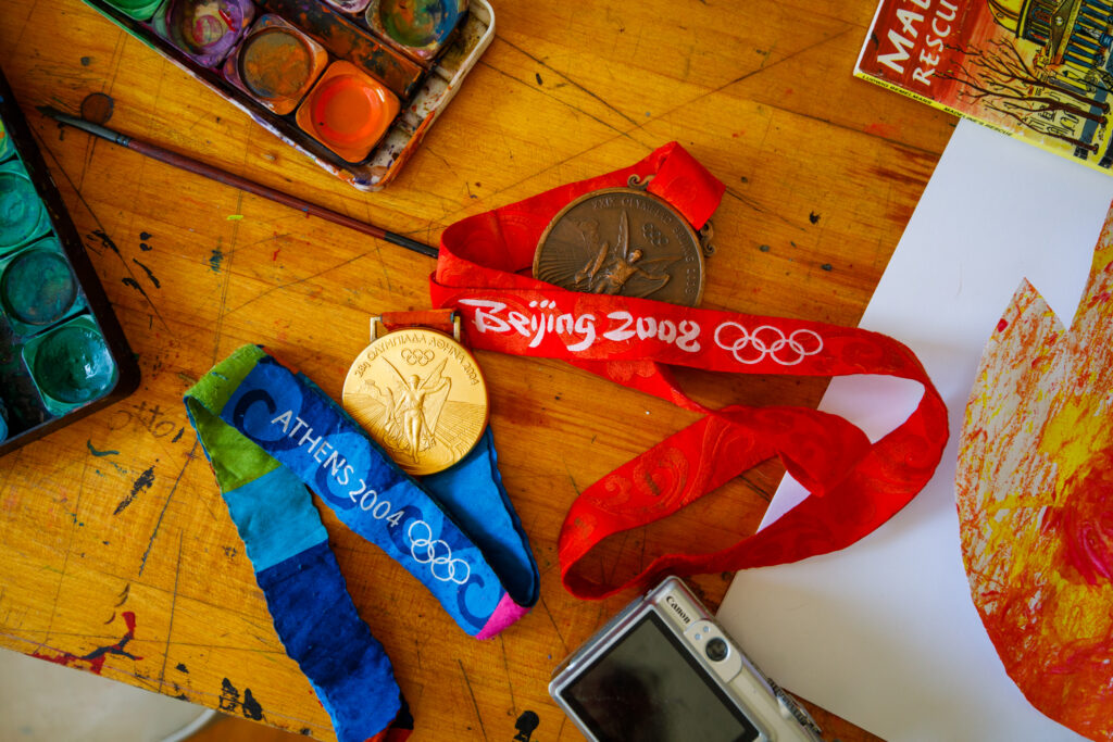 Two gold Olympic medals sit next to watercolor paint and paper on a kitchen table.