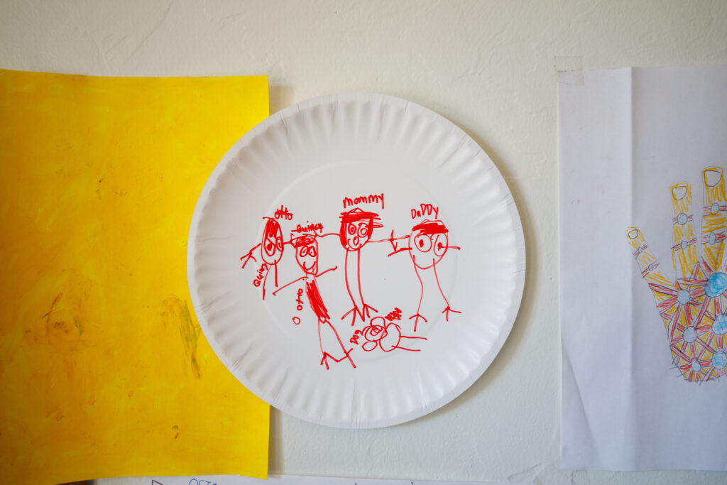 Paper plate craft pinned to the wall with a child's drawing of family in red marker. 