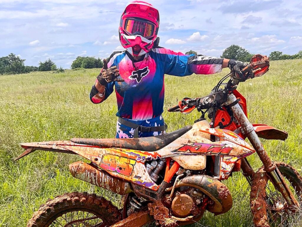Ashley Saunders in full dirt bike riding gear standing with a dirt bike.