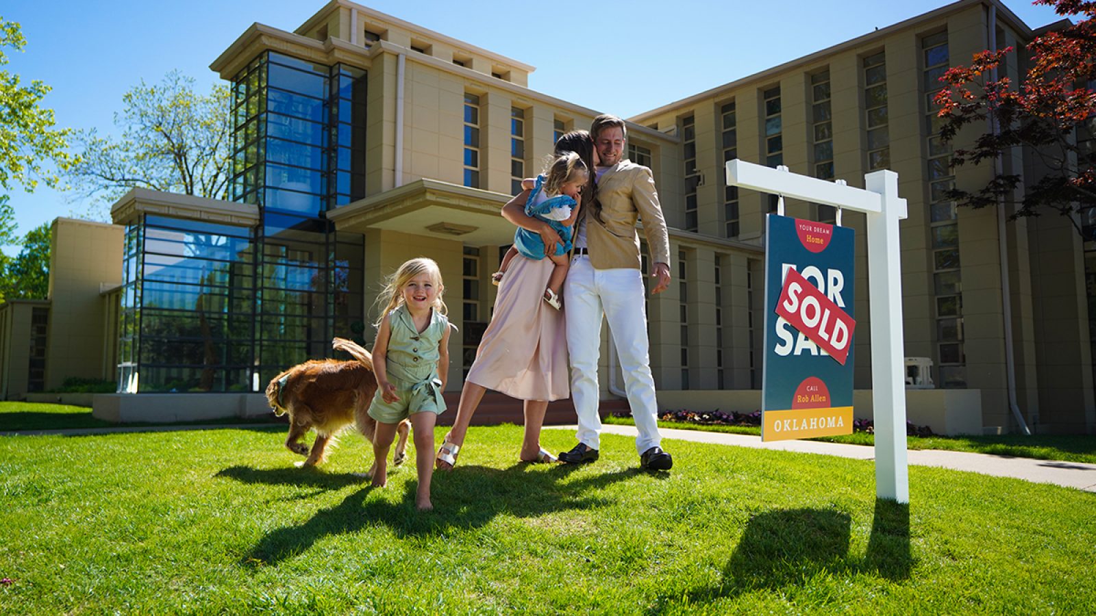 Family with young children and dog play in front yard of a home with a yard sign that says "sold".