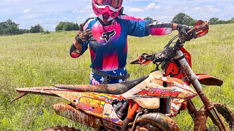Ashley Saunders in full dirt bike riding gear standing with a dirt bike.